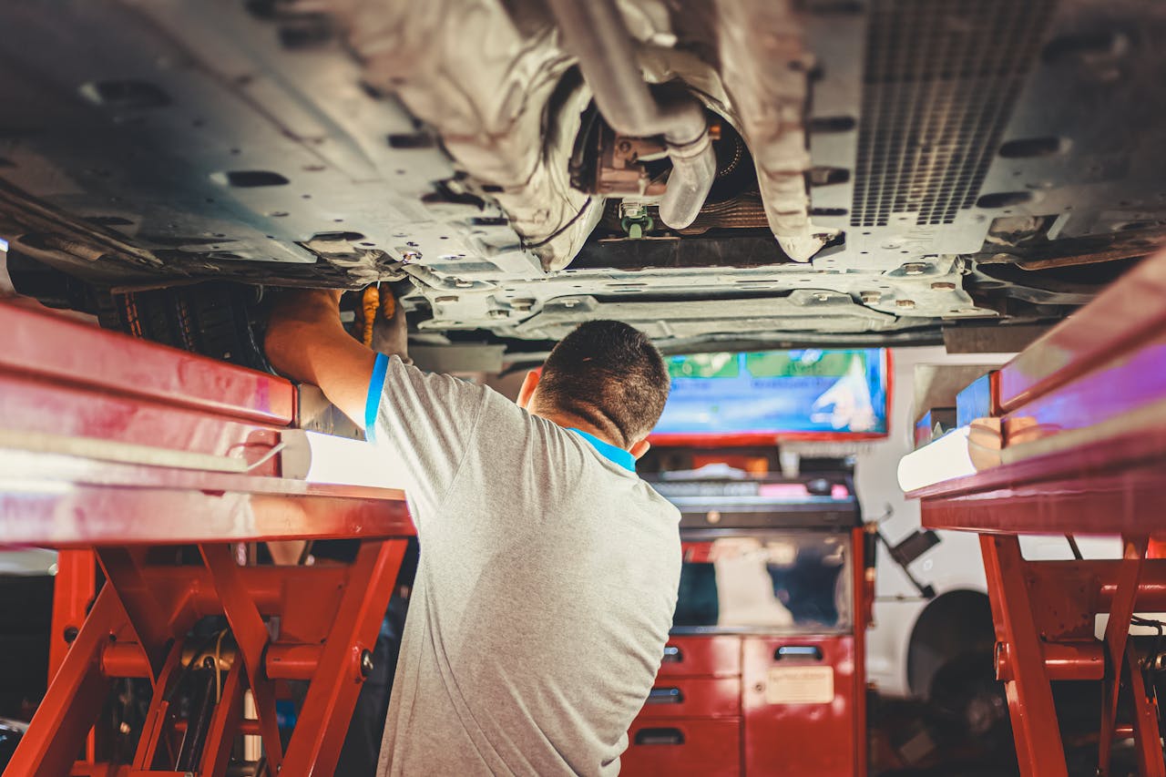 Home A mechanic works under a lifted car in an auto repair shop, adjusting parts.