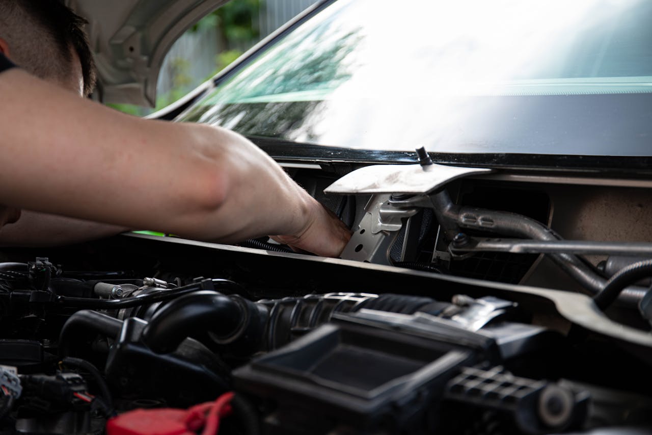 Home Mechanic performing engine maintenance on a car outdoors, focusing on repair work.